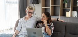 Happy couple talking and looking on laptop together in the living room