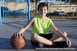 Young smiling basketball player sitting on the court 0vvgp0