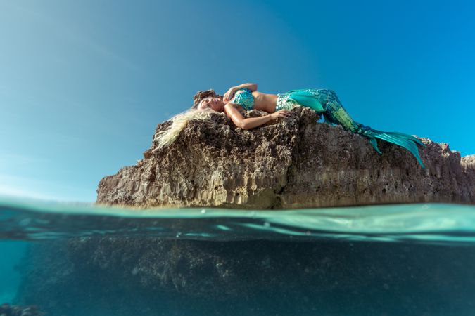 Blond fairytale female mermaid lying on rock