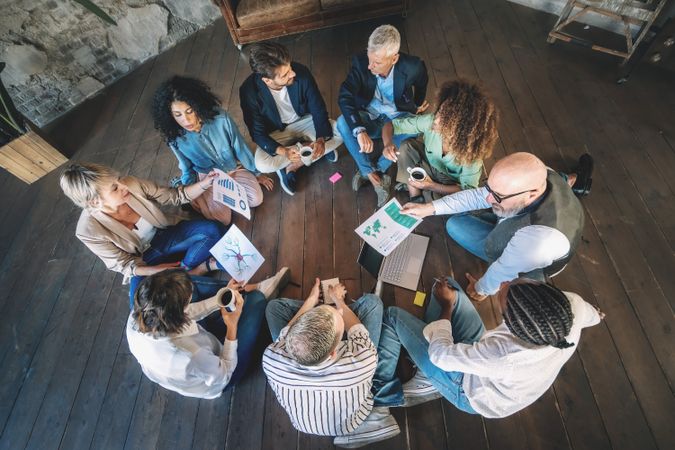 A diverse group of professionals engage in a creative brainstorming session, seated on the floor and sharing ideas