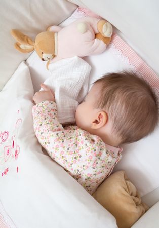 Newborn sleeping in a cot with pacifier and toy