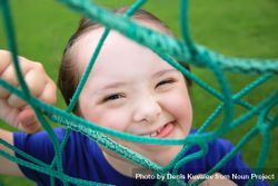 Close up portrait of little girl looking at camera framed by playground net 56k3j4