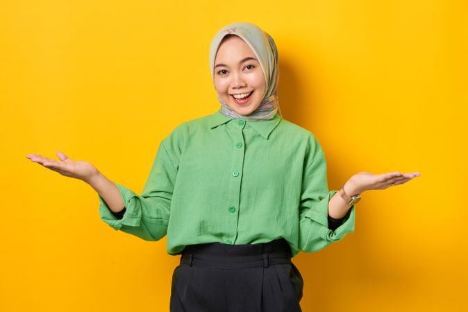 Smiling Muslim woman in headscarf and green blouse with both palms up