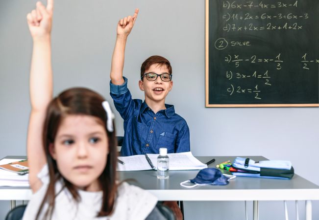 Students with mask on table raising hands at school
