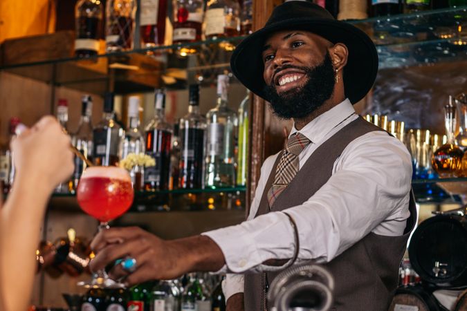 stylish Black bartender offering a customer a cocktail decorated with garnish in a traditional cocktail bar
