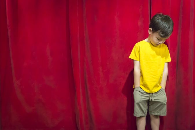 Pouting Biracial Boy Standing In Front of Red Curtain