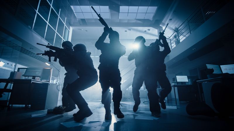 Masked Team of Armed SWAT Police Officers Move in a Hall of a Dark Seized Office Building with Desks and Computers.