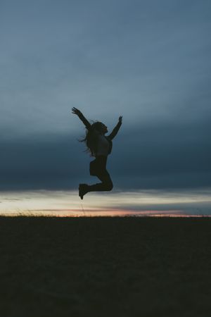 Silhouette of a woman jumping in a field with her arms up and knees bent