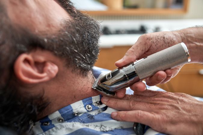 Crop barber trimming beard of male client