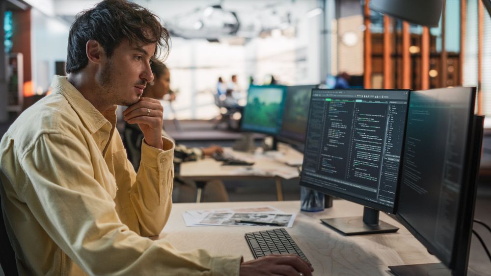 Male Game Programmer Coding On Desktop Computer In Game Design Studio Diverse Office.