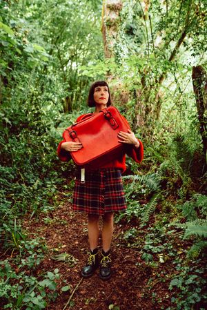 Woman in red with big red suitcase in forest