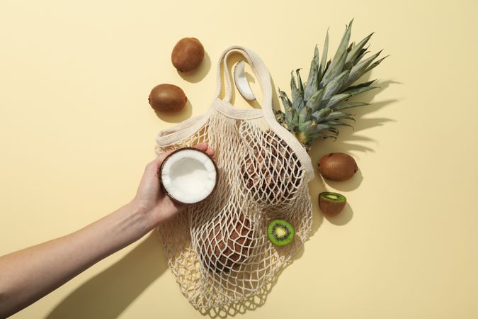 Set of tropical fruit in bag and hand on beige background, top view