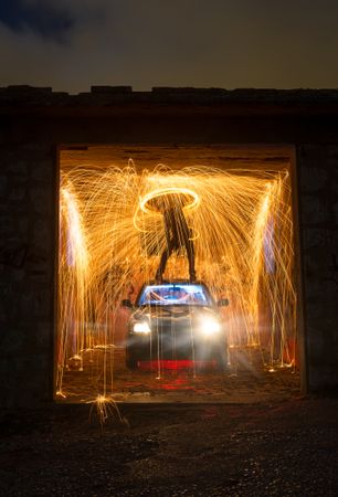 Person with burning round on car in garage in darkness