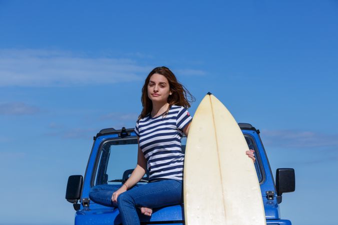Woman sitting on top of a car with surfboard