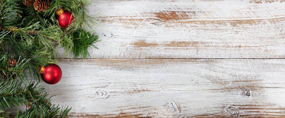 Christmas background with border of fir branches and red ball ornaments on rustic wooden background