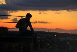 Out line of male sitting on roof against a colorful dusk side