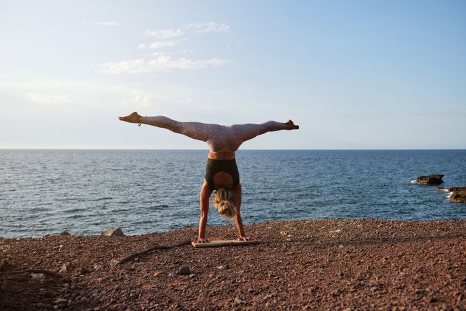 Woman doing the handstand yoga position in front of the sea