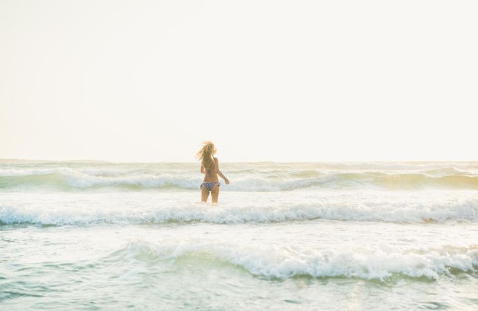 Rear shot of long haired woman in bikini in waves at the beach