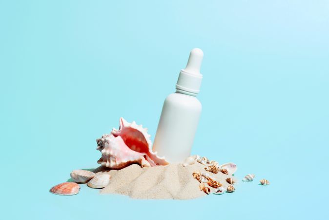 Pile of sand with seashells and cosmetic bottle