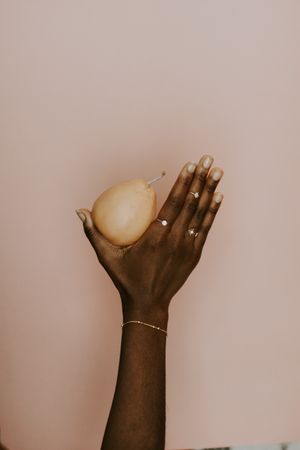 Black hand holding a pear wearing a gold jewelry