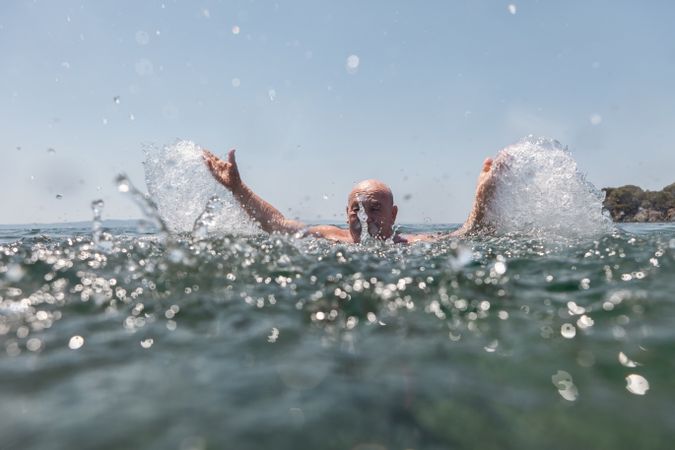 Active mature man swimming and splashing in water