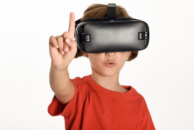Little girl looking in VR glasses and gesturing with finger pointing up