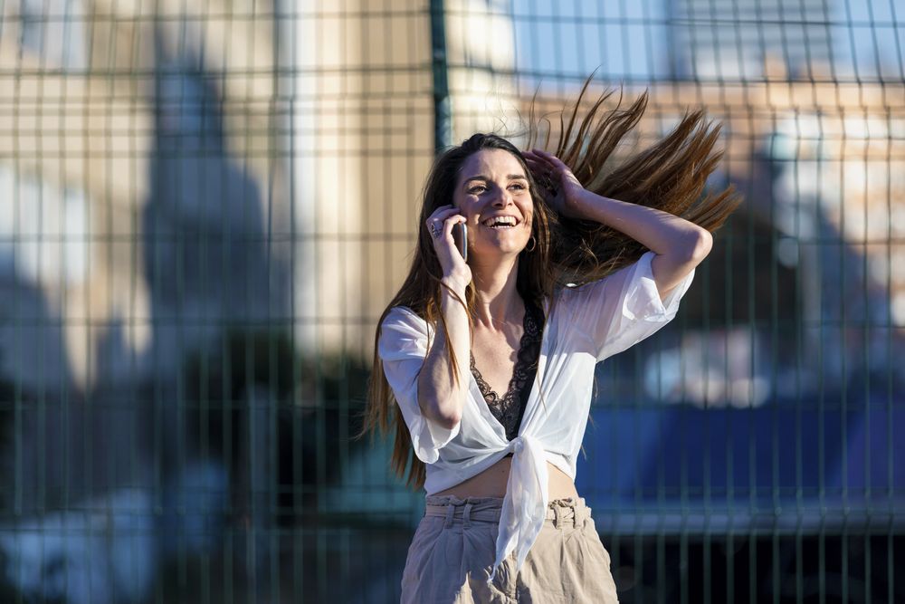 Happy young woman standing in the street while using a mobile phone