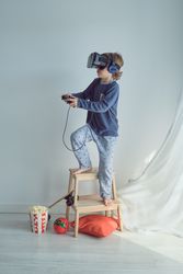 Curious boy in VR glasses and headphones playing with joystick