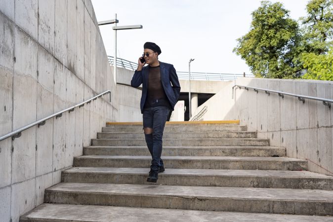 Young Latino man wearing a fashionable hat and sunglasses, walking down the stairway while texting on his smartphone