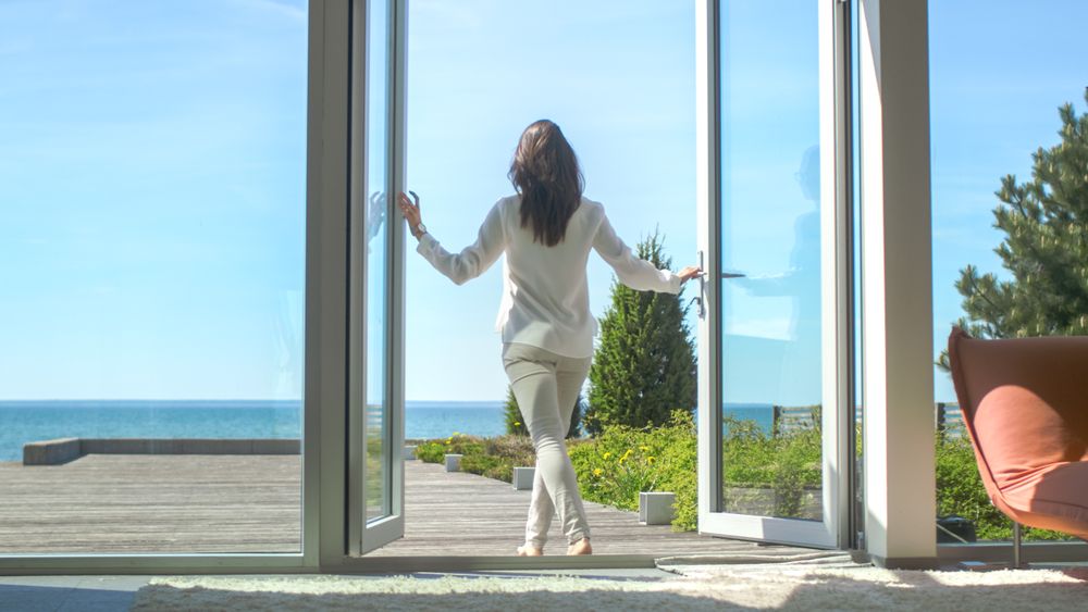 Shot of a Brunette with Loose Hair Opening Doors of the Balcony and Walking onto Sunny Terrace with Seaside View.