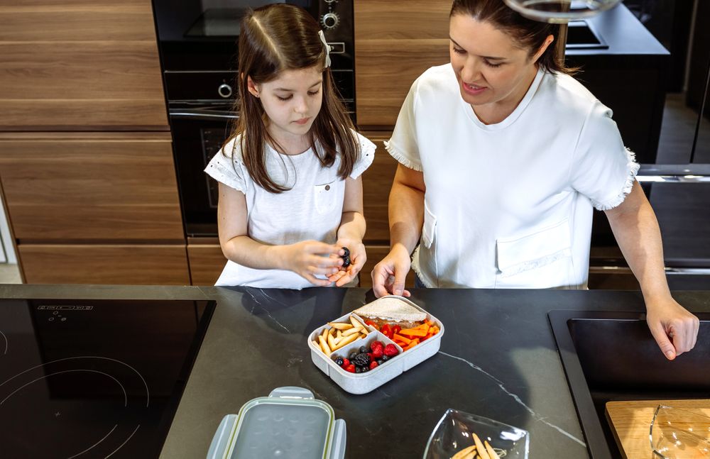 Mother watching her daughter put food in her lunch box