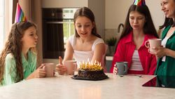 Girl blowing out candles on birthday cake surrounded by family.