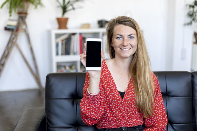 Smiling woman showing a screen of a smart phone while sitting on a sofa