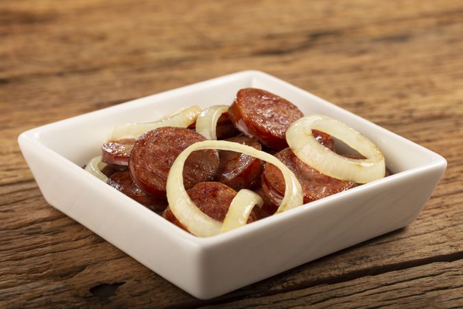 Sliced calabrese sausage with onion on wooden background.