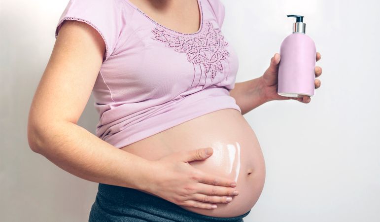 Pregnant woman applying anti-stretch mark cream