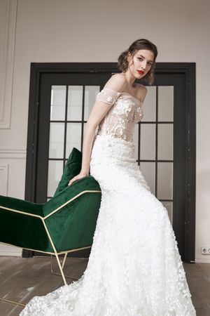 Chic calm woman in white wedding dress leaning on armchair