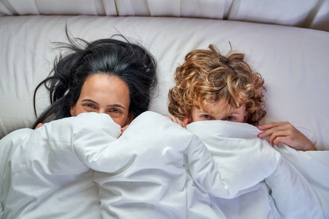 Mom and little son lying on bed covered with blanket