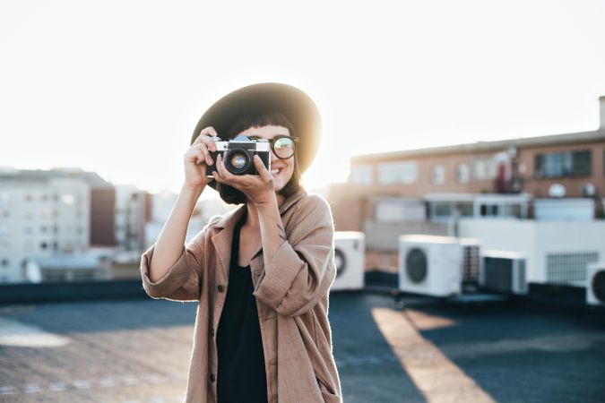 Trendy woman with camera taking picture outside at sunset