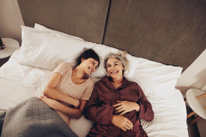 Happy woman lying beside her mother on bed laughing and smiling