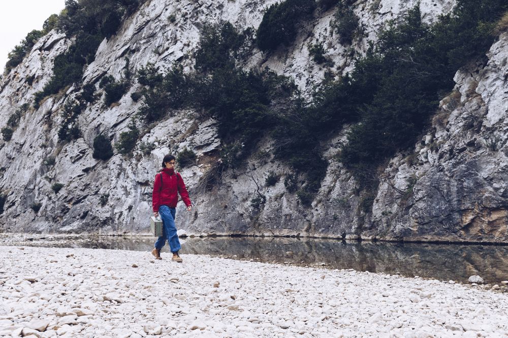 Woman with case walking on shore above stream