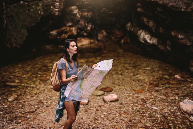 Young woman hiking in mountains and reading a map for directions