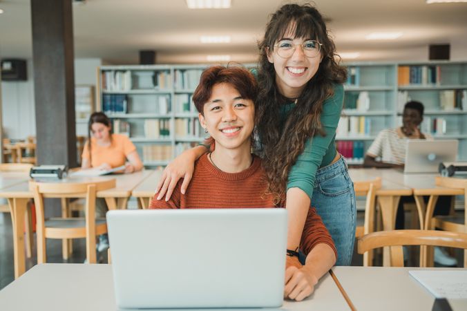 Cheerful diverse students with laptop in library