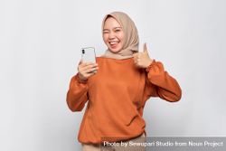 Happy Muslim woman in headscarf and orange shirt pointing at phone 5reR30