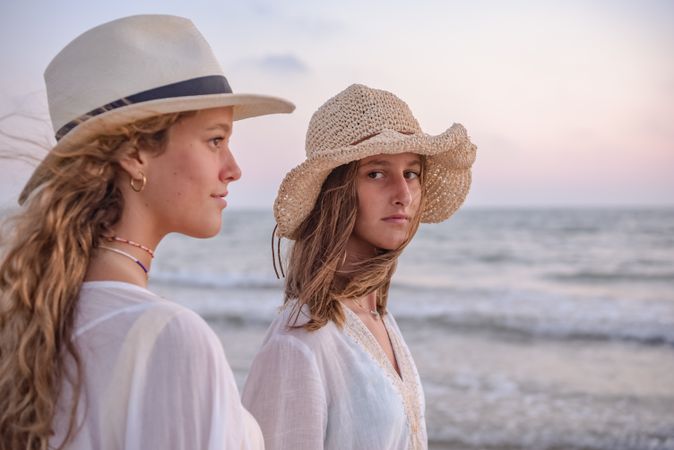 Smiling girlfriends in summer clothes barefoot in water on beach