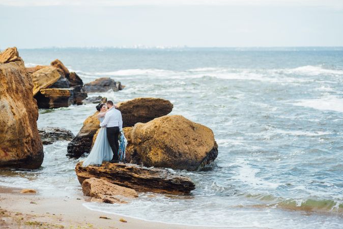 Man and woman hugging and standing on rock at the beach