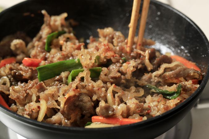 Chopsticks in wok with stir fry of beef and glass noodles
