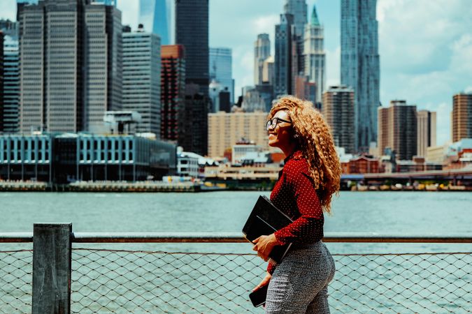Smiling professional Black female walking along the Hudson River with Manhattan in the background