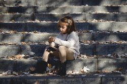 Child sitting on cement steps in outdoor park with fall leaves