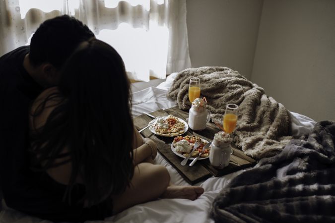 Young couple near appetizing waffles and tasty drinks on tray on bed