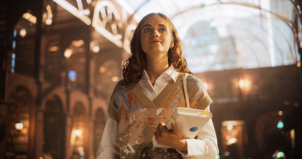 Young Female Student Holding Books in a Bustling Train Station. Intelligent Woman with Curly Hair